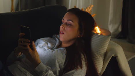 Woman-Lying-On-Sofa-At-Home-At-Night-Streaming-Or-Looking-At-Online-Content-On-Mobile-Phone-1